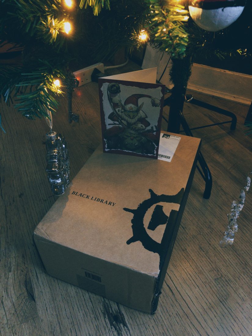 A cardboard box, with the Black Library logo on it, underneath a Christmas Tree